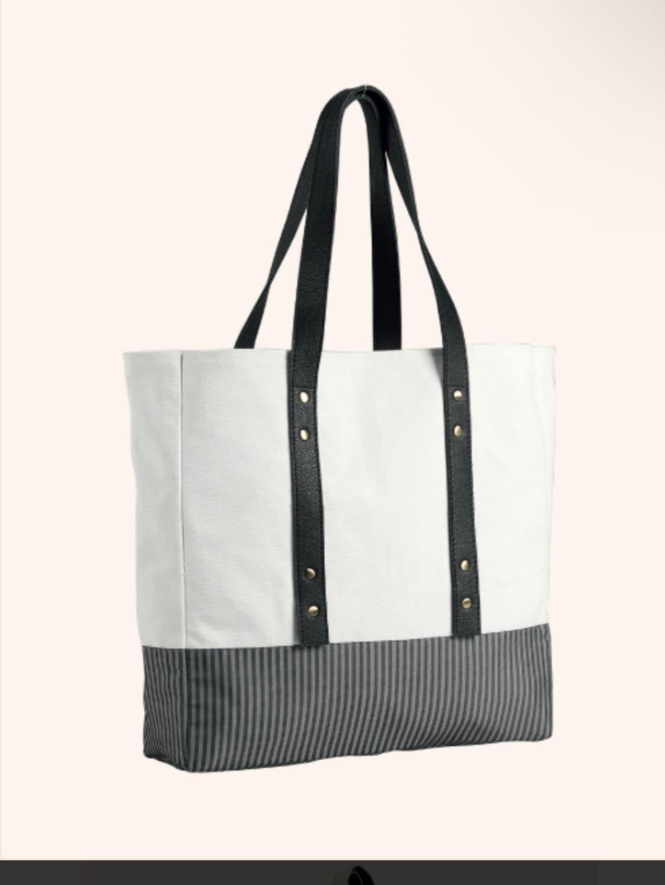A canvas tote bag with a white upper section, a dark gray and white vertically striped bottom panel, and black shoulder straps with gold-tone rivets, shown against a light beige background.