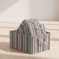 A stack of three fabric storage bins with a colorful vertical stripe pattern in red, green, blue, and gray, featuring cream-colored rope handles, set against a solid off-white background.