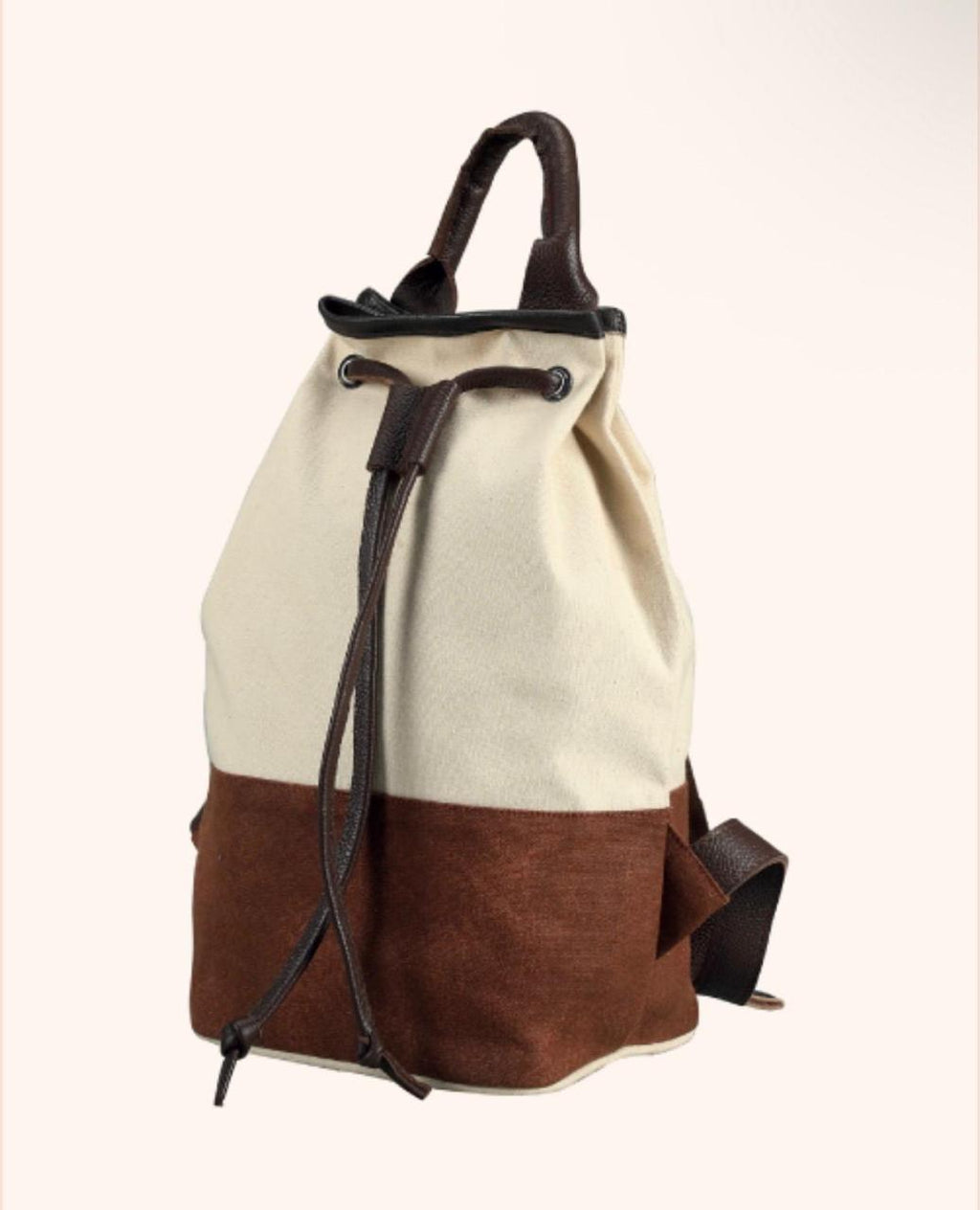 A two-tone canvas backpack with an off-white upper section and a brown lower section, featuring dark brown leather handles, drawstring closure, and side strap on a light cream background.