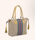 A beige woven tote bag with tan leather handles and trim, featuring a colorful striped textile panel on the front. The bag has gold-tone metal hardware and tassel details on the sides, shown against a light beige background.