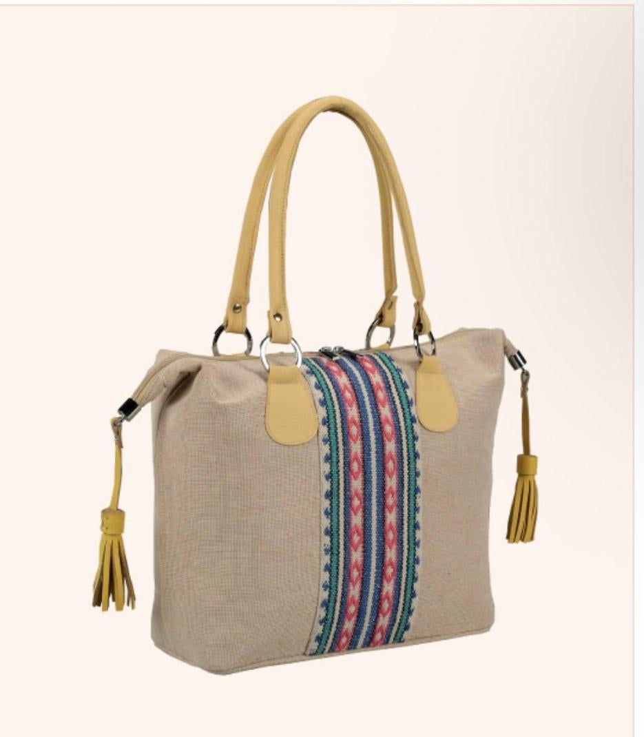 A beige woven tote bag with tan leather handles and trim, featuring a colorful striped textile panel on the front. The bag has gold-tone metal hardware and tassel details on the sides, shown against a light beige background.