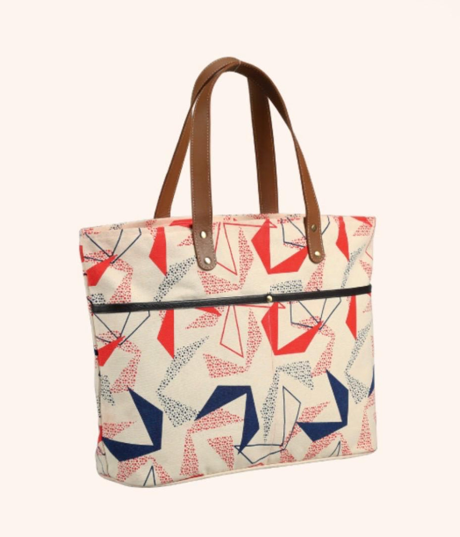 A tote bag with a cream canvas body featuring a red, navy, and gray geometric pattern, brown leather handles, and a black zipper on the front pocket. The image is set against a light beige background with a white strip at the bottom containing the text 'POL/CS-021'.